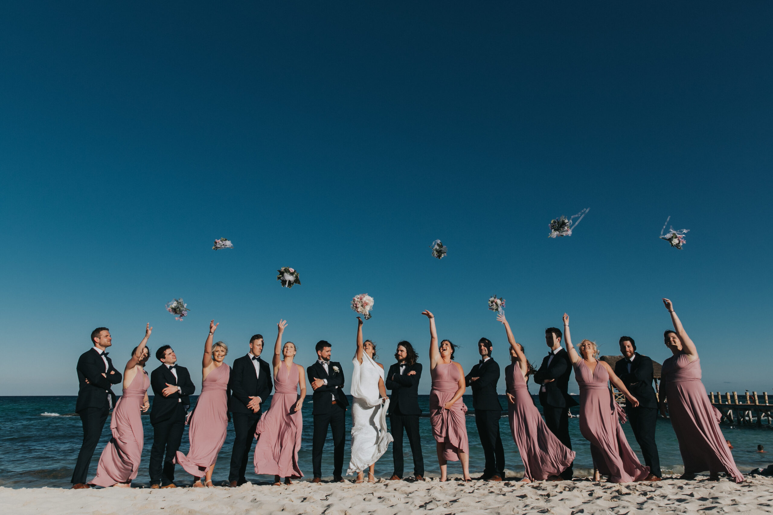 Wedding party toss bouquets into air on Azul Fives beach