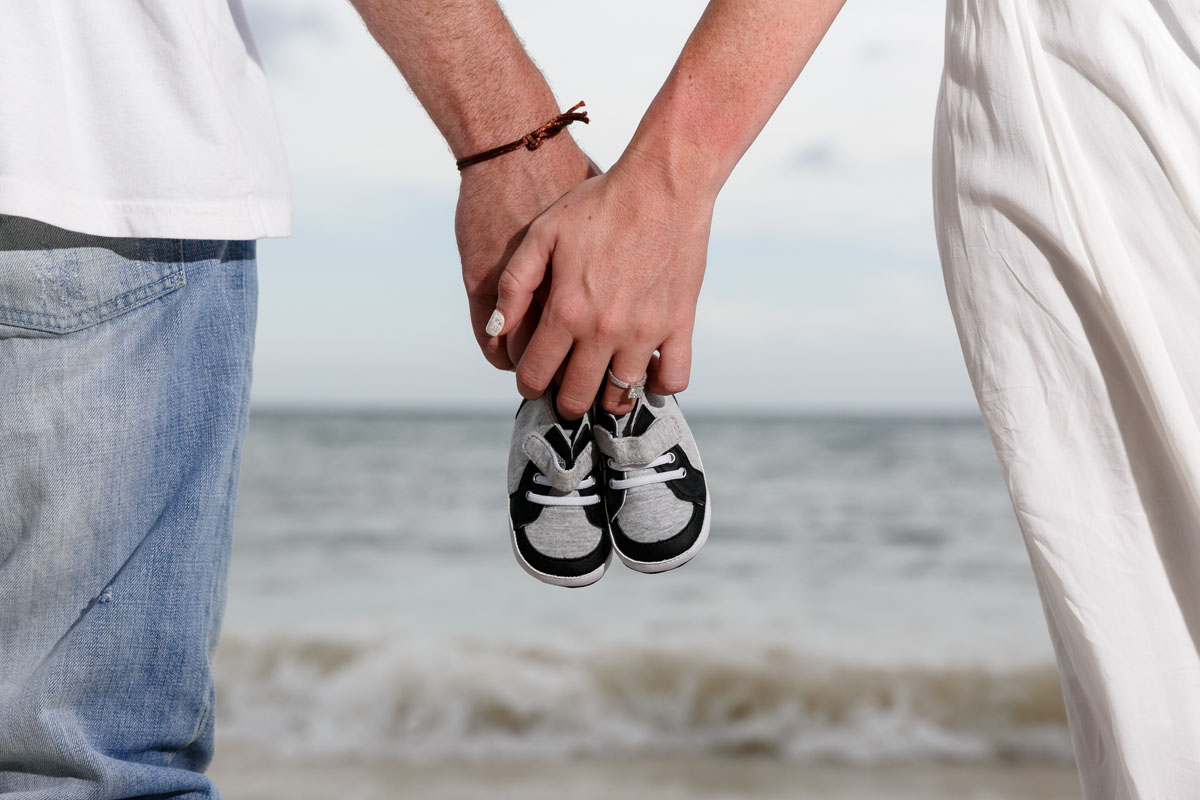 Newy engaged couple at the beach hold baby shoes