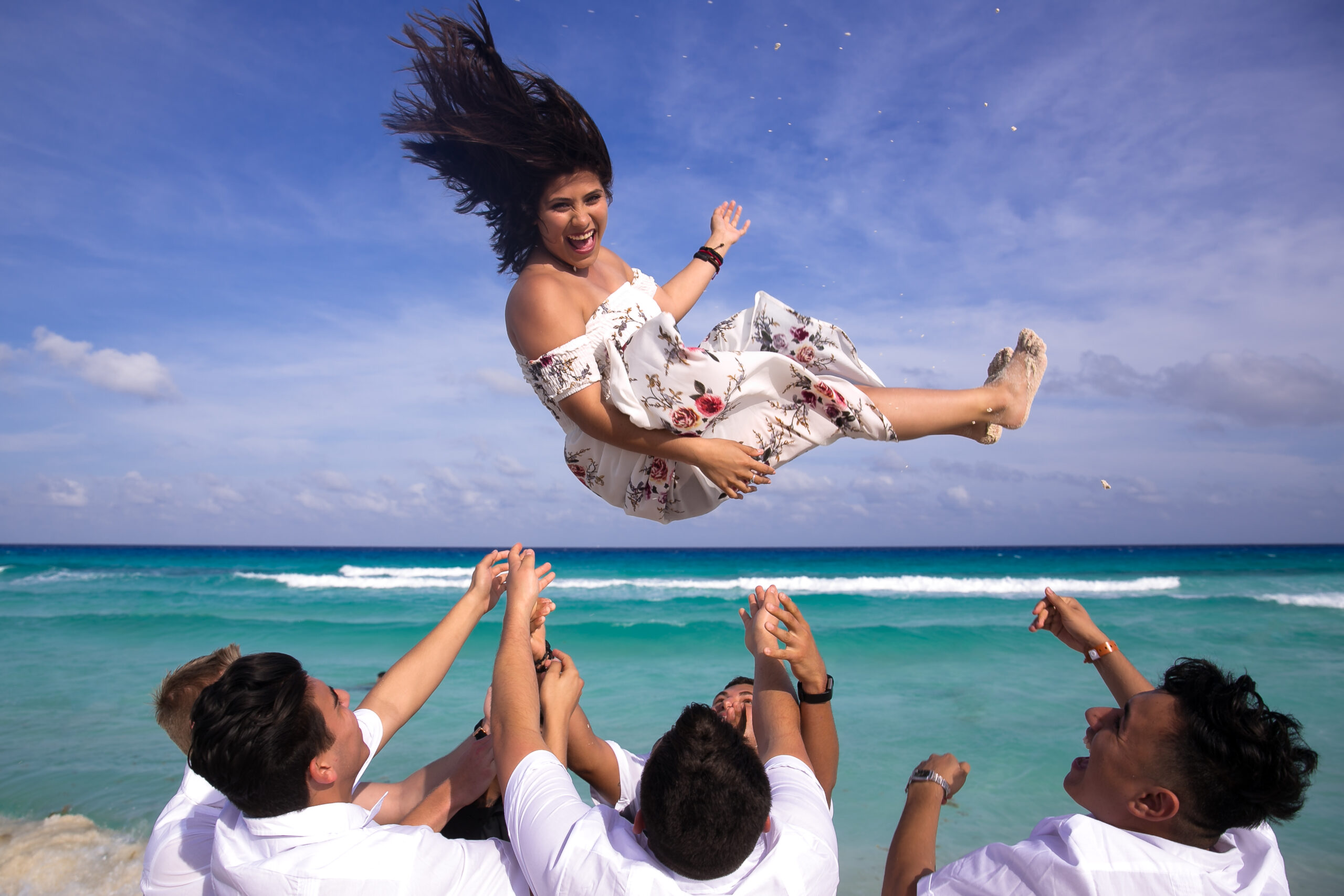 Friends throwing birthday girl in the air at Cancun beach