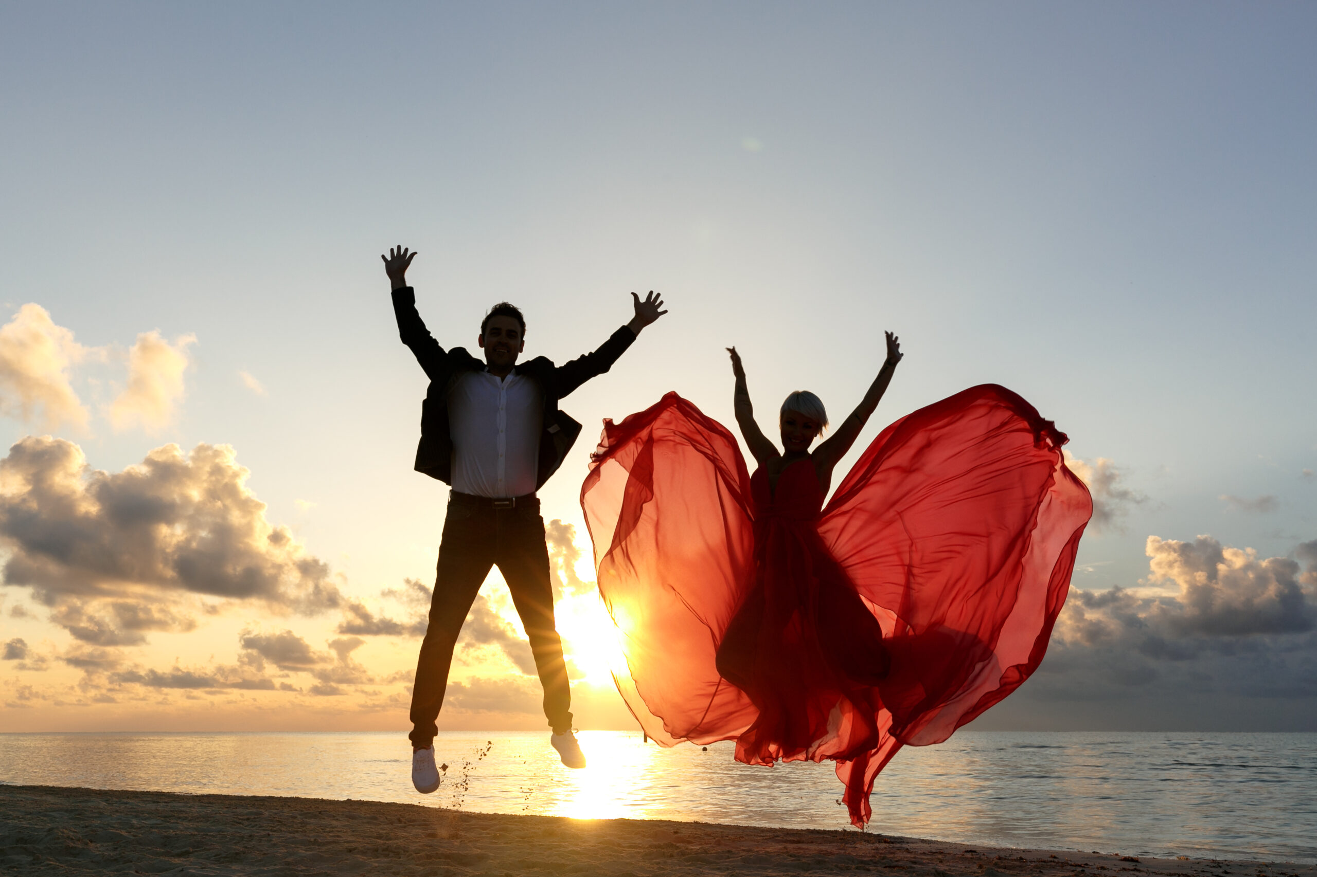 Sunrise shilouette couple jumps for joy on beach