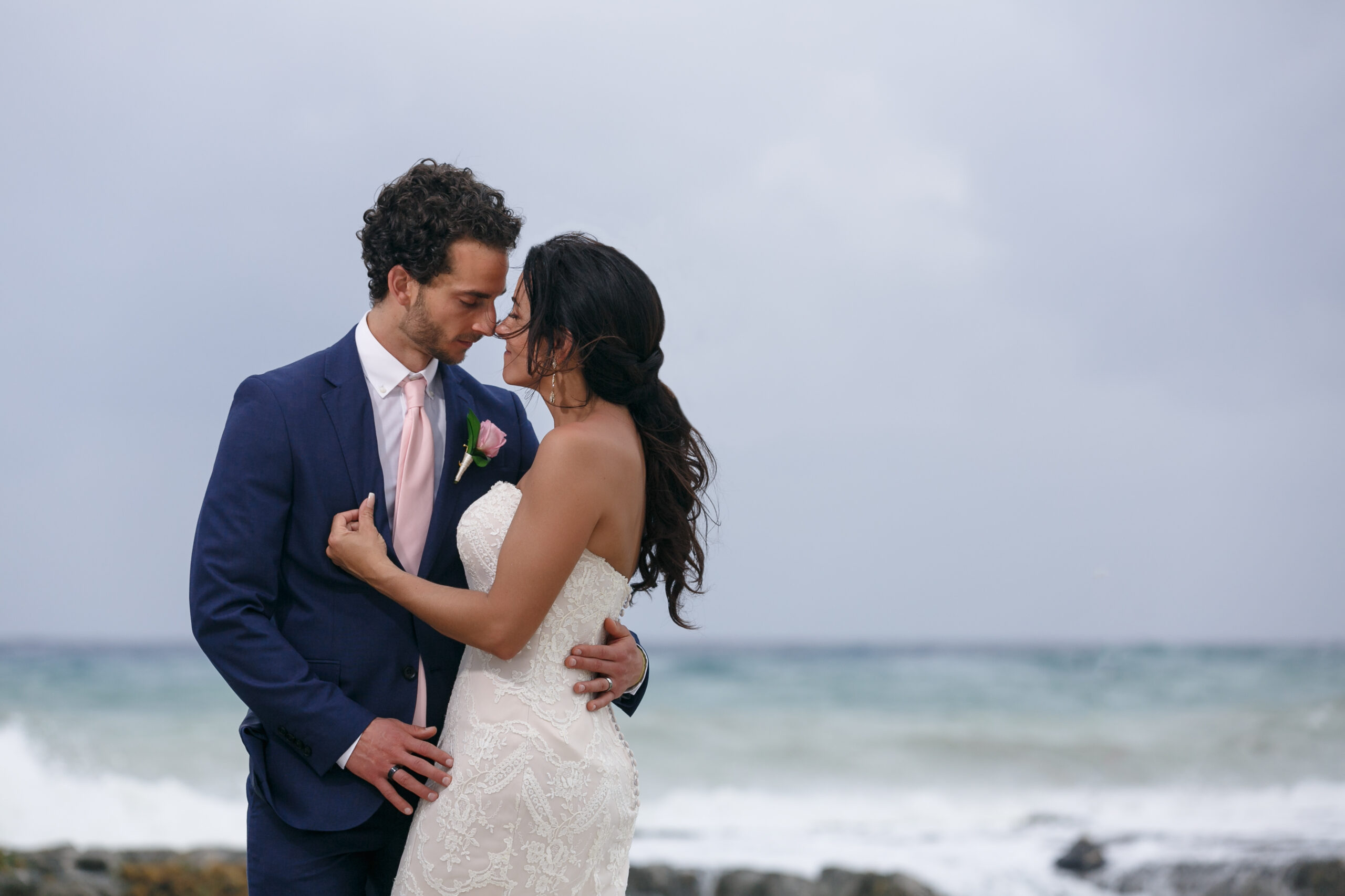 Newlyweds embrace on windswept rock at Hard Rock Riviera Maya