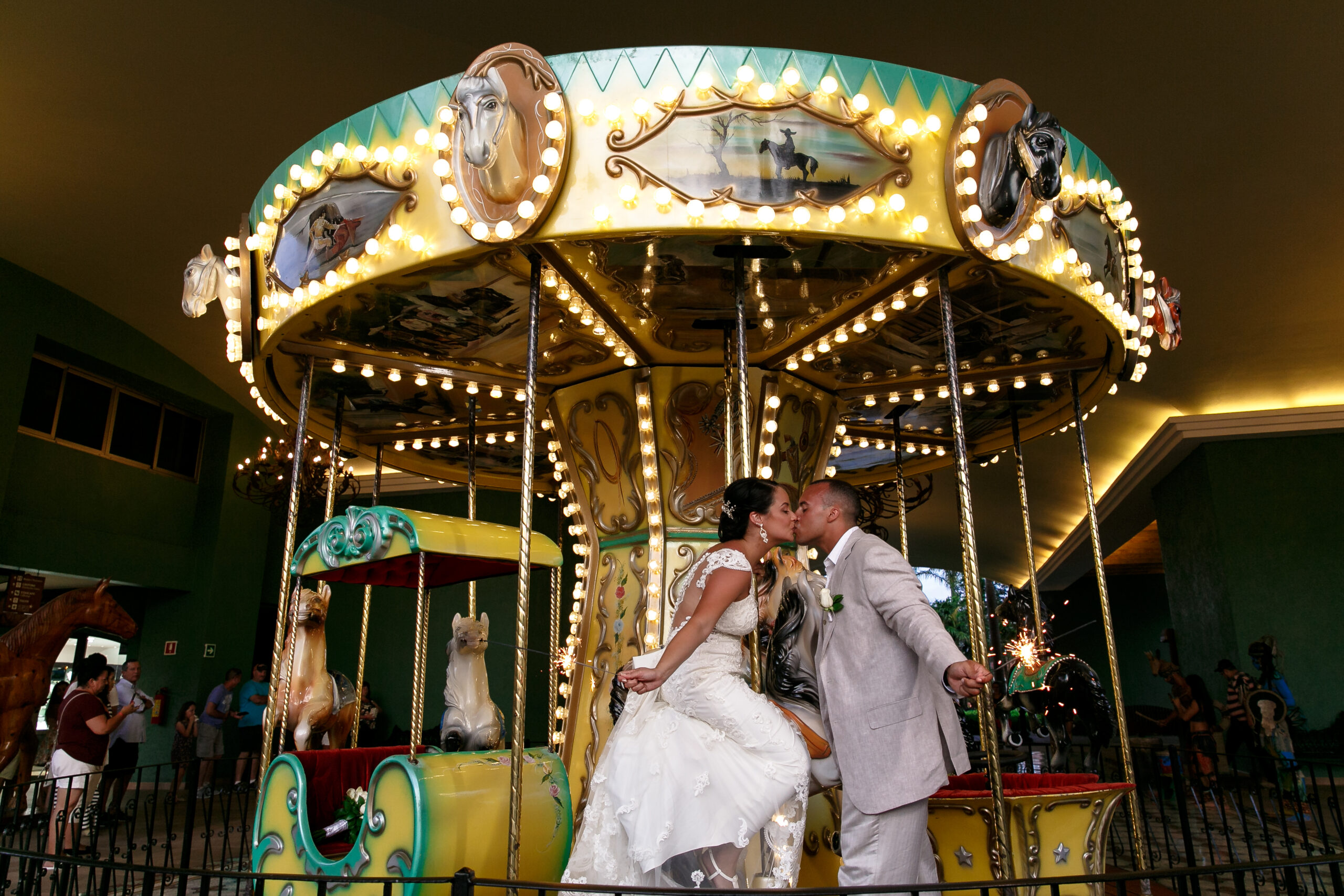 Newlyweds kiss under merry-go-round canopy, riding on a pony