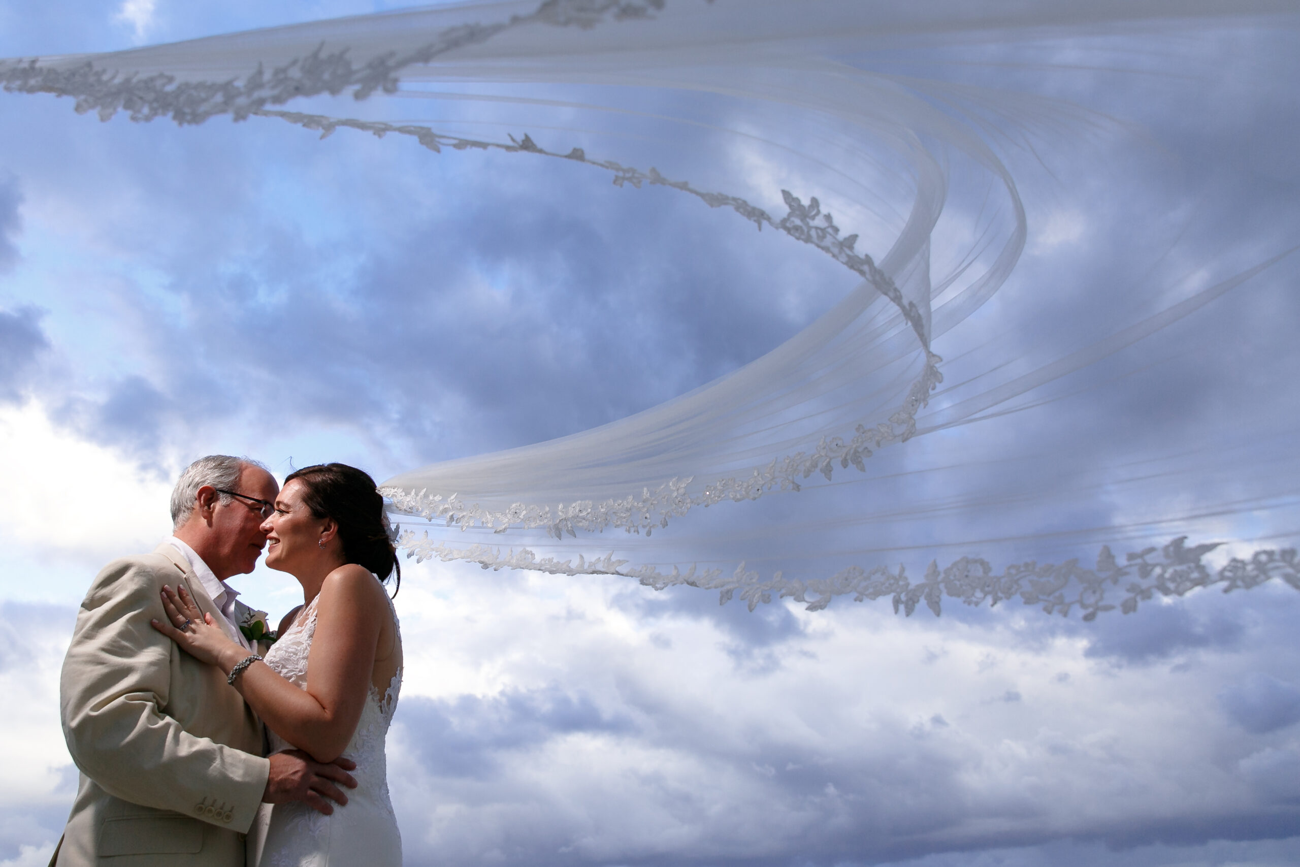 Newlyweds embrace on the beach under bride's billowing veil