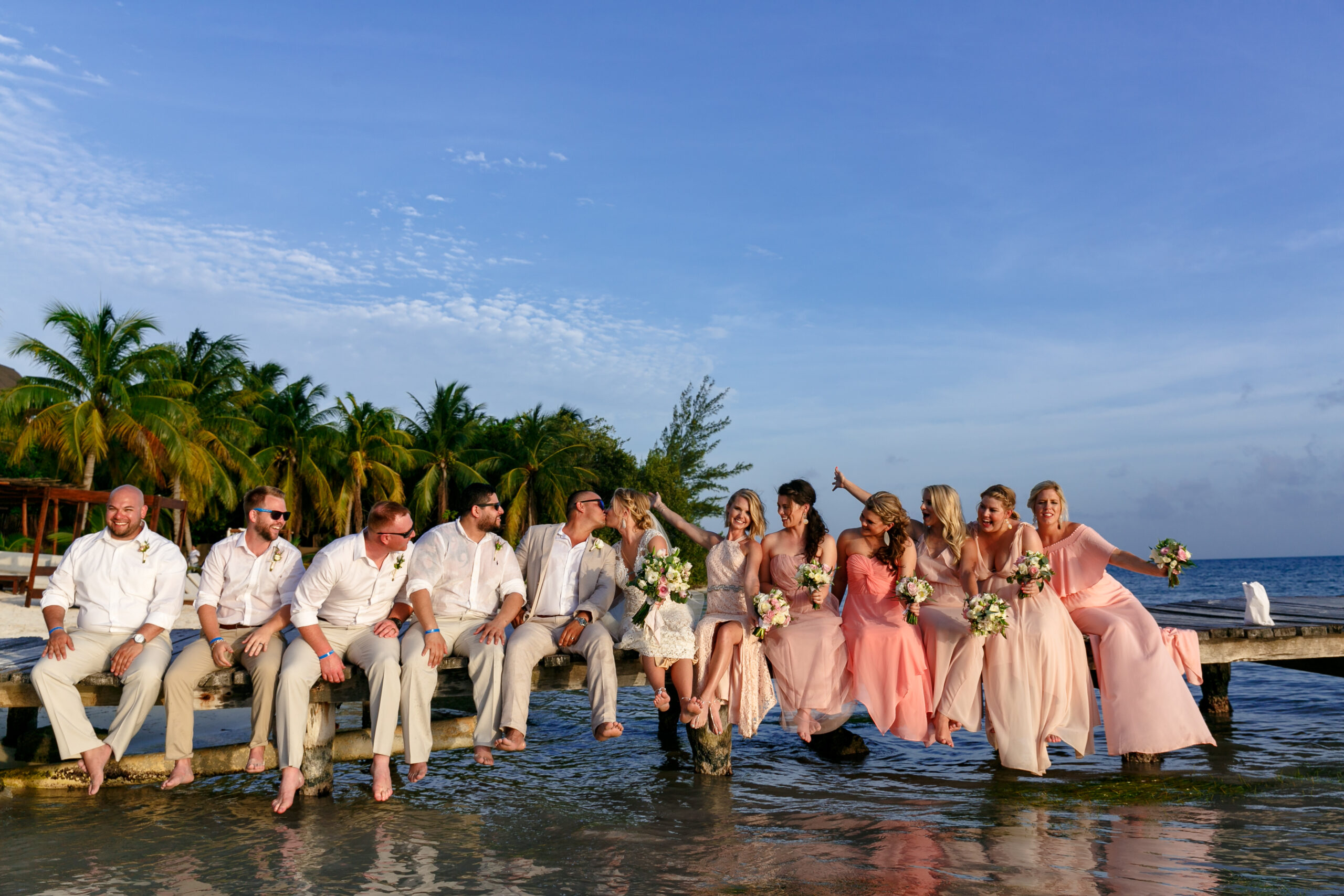 Newlyweds kiss on dock surrounded by their weddng party