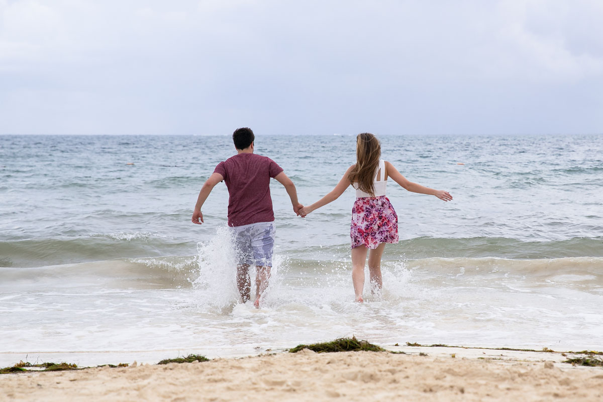 Newly engaged couple splash in the ocean, holding hands