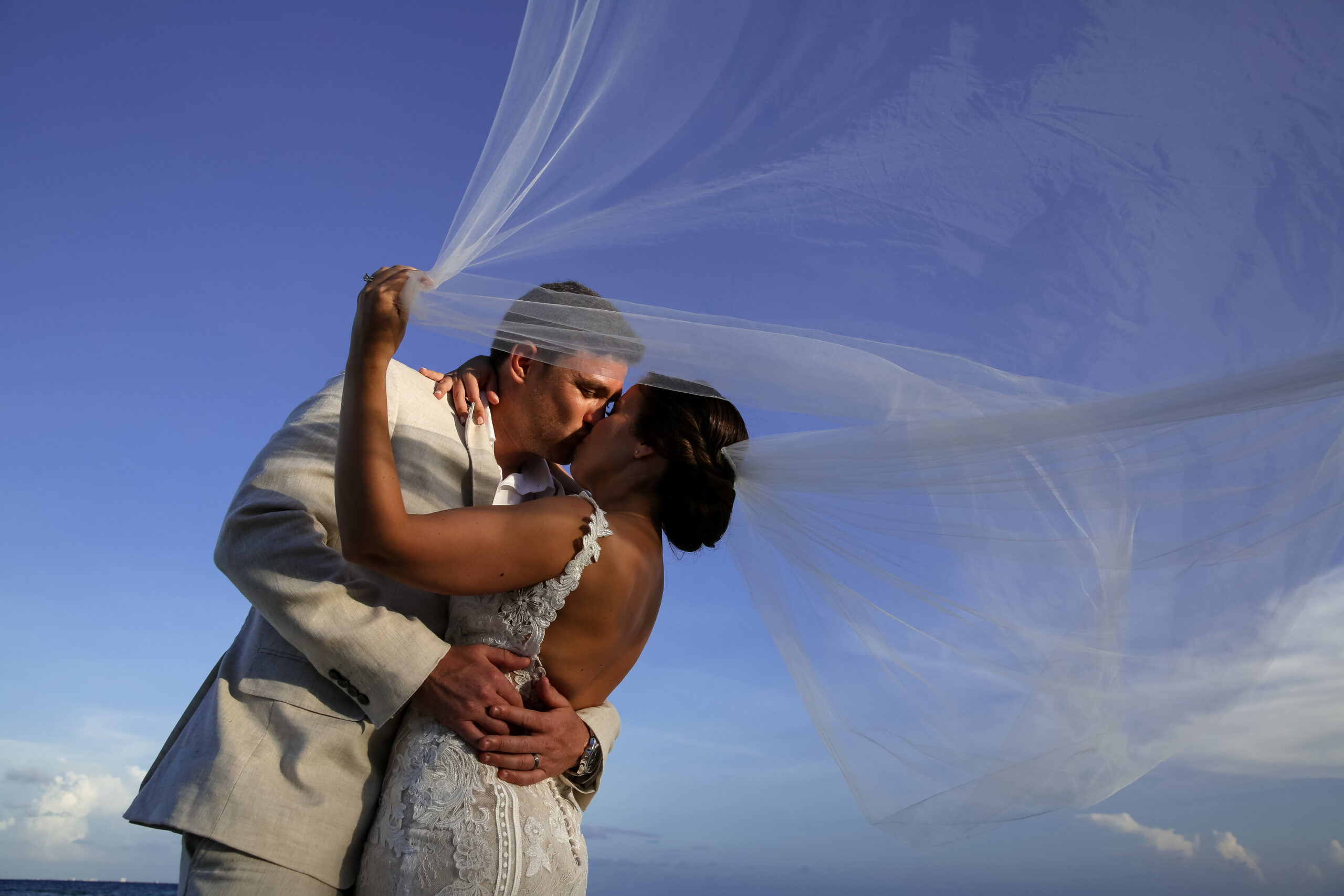 Newlyweds kiss on the beach under the bride's billowing veil