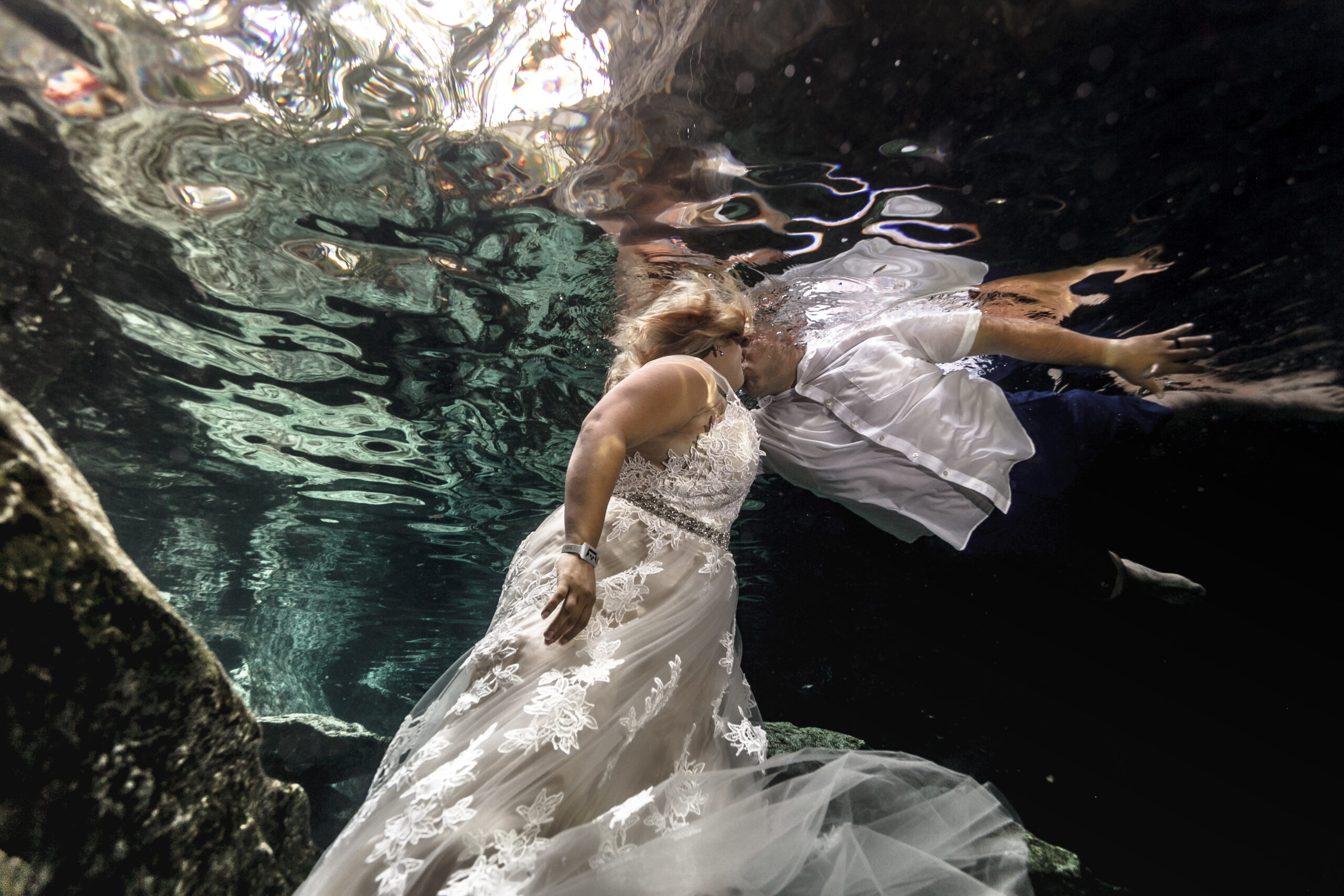 Anniversary couple kiss underwater in crystal clear water of a jungle cenote