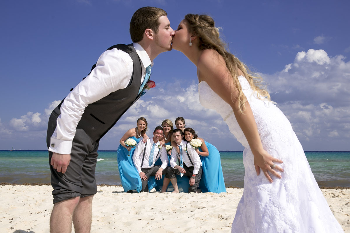 Wedding couple kissing on the beach with attendants in the background