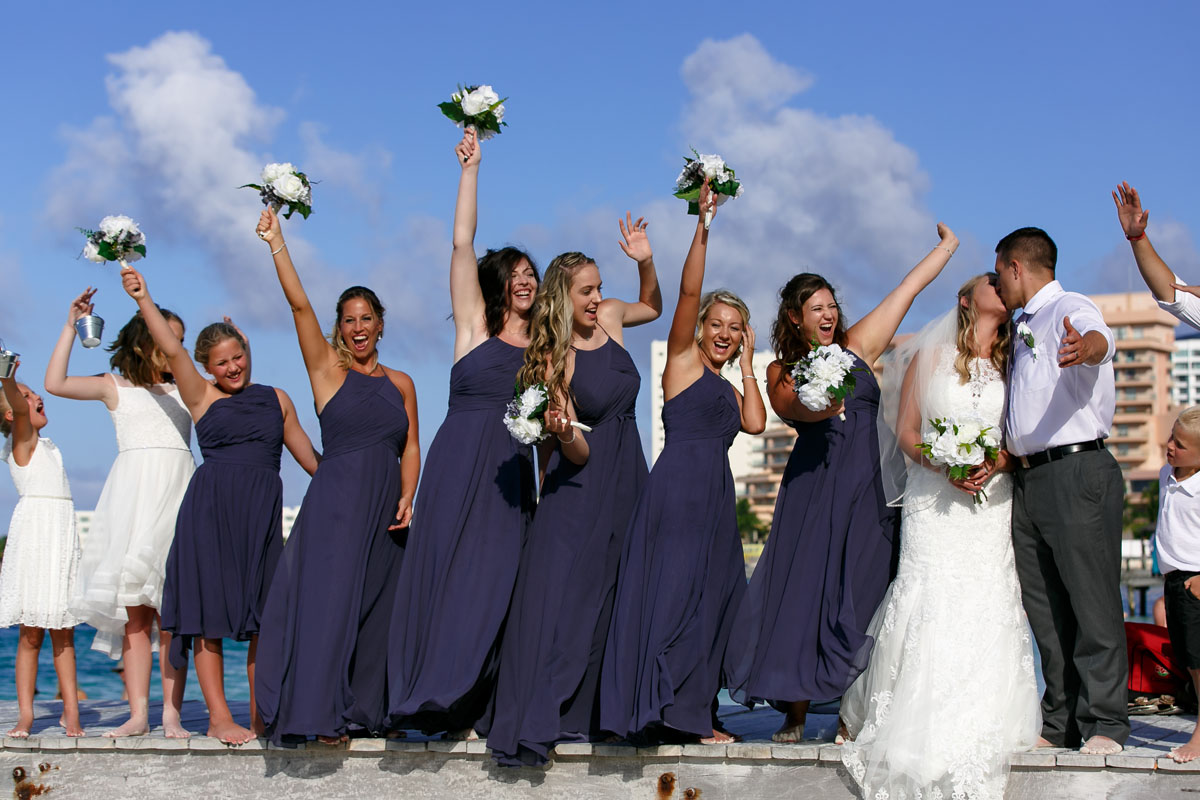 Newlyweds kiss on pier with cheering wedding party