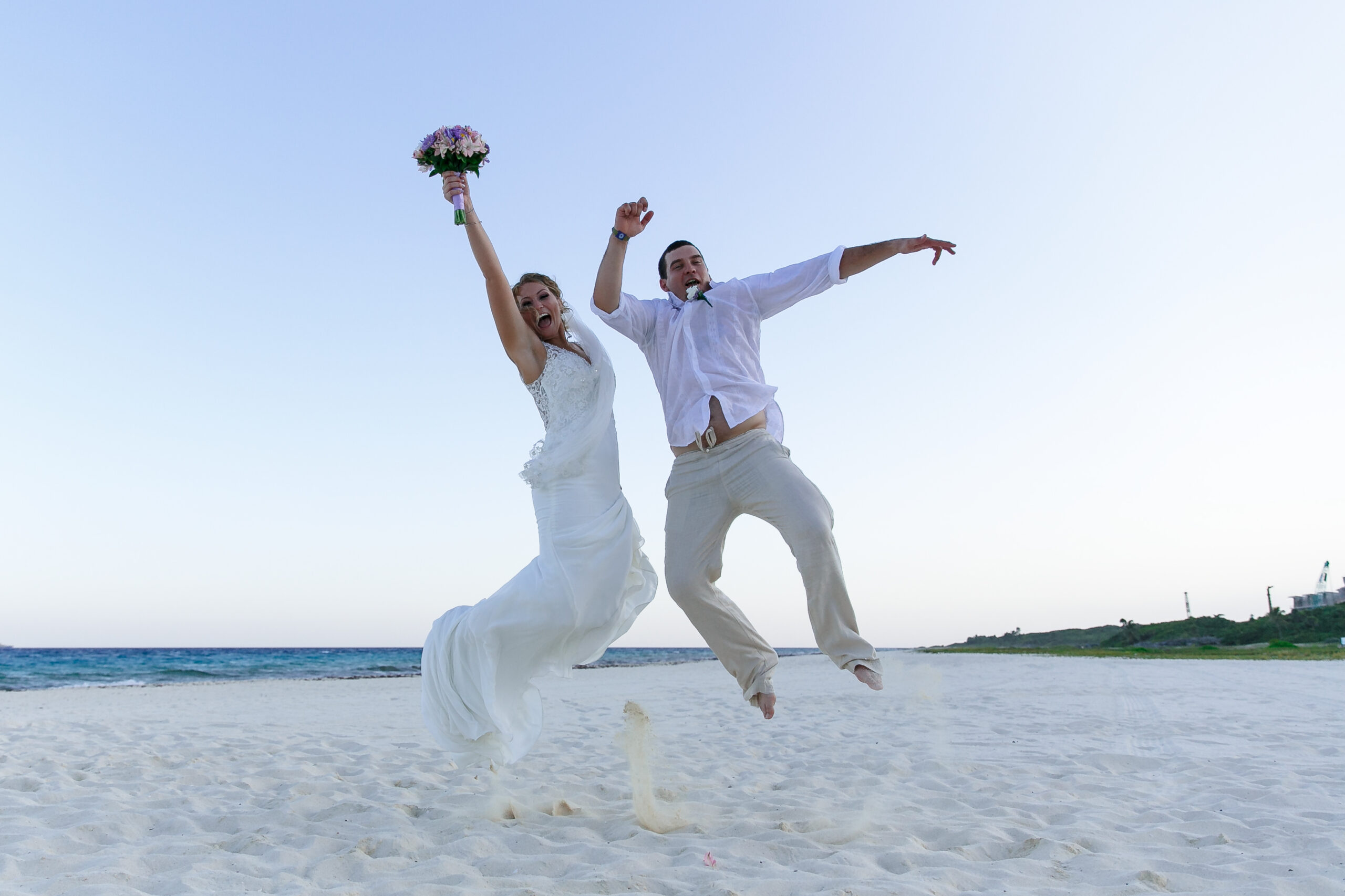 Overjoyed newlyweds jump for joy on white Sandos Playacar beach