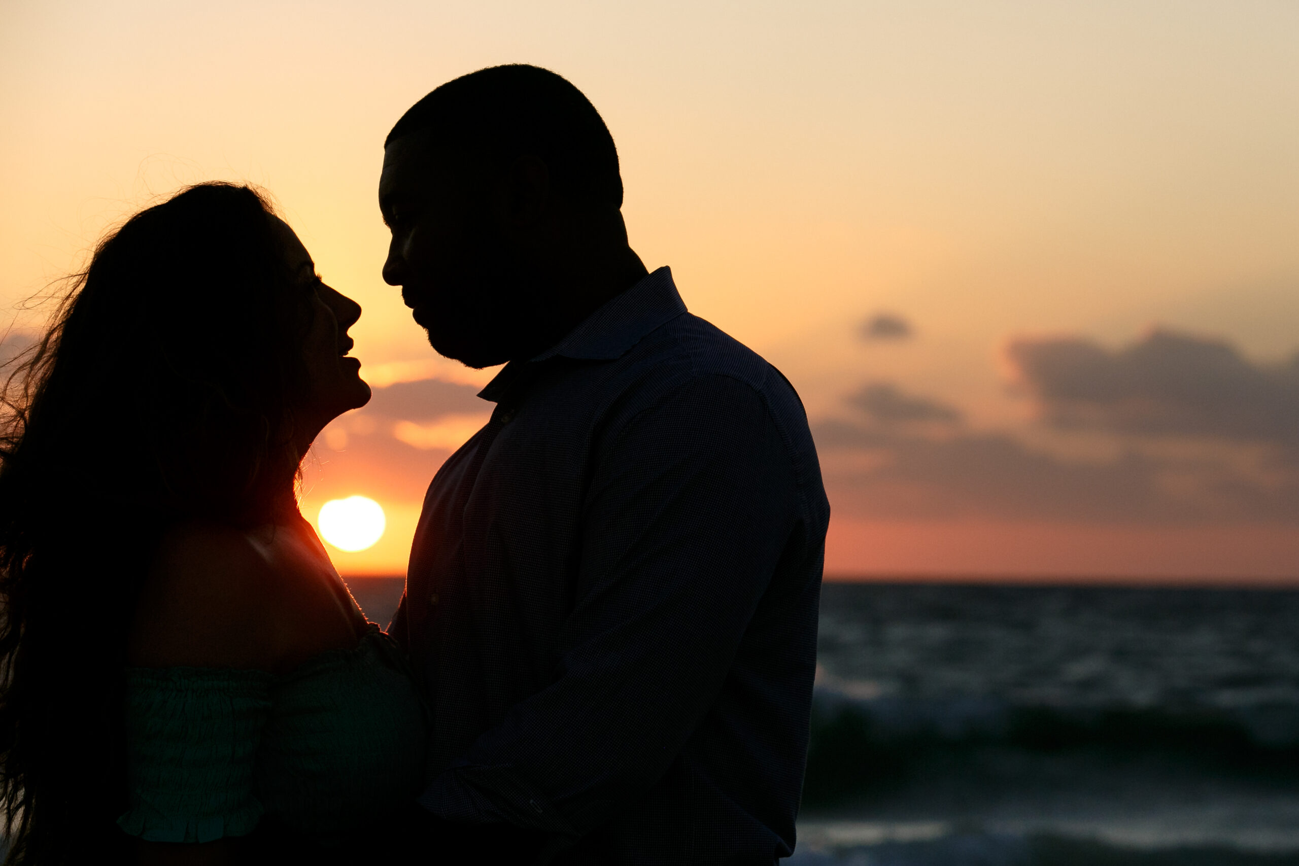 Engaged couple's silhouette against sun setting over ocean