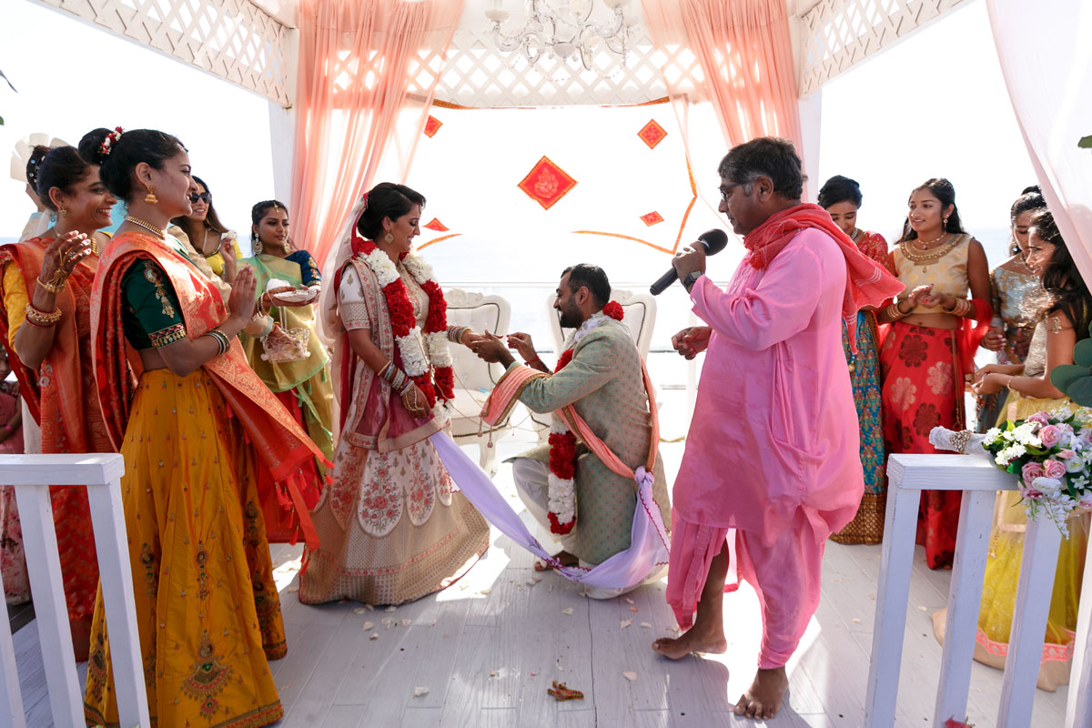 Groom kneels before his bride as he puts ring on her finger