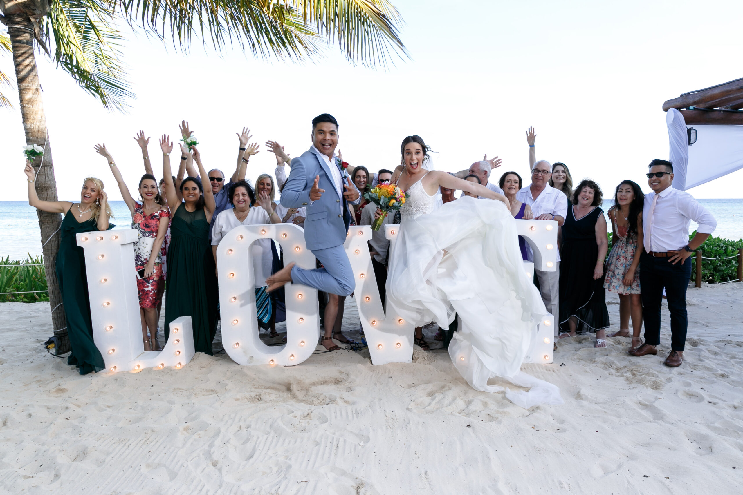 Newlyweds jump for joy in front of their guests by a LOVE sign