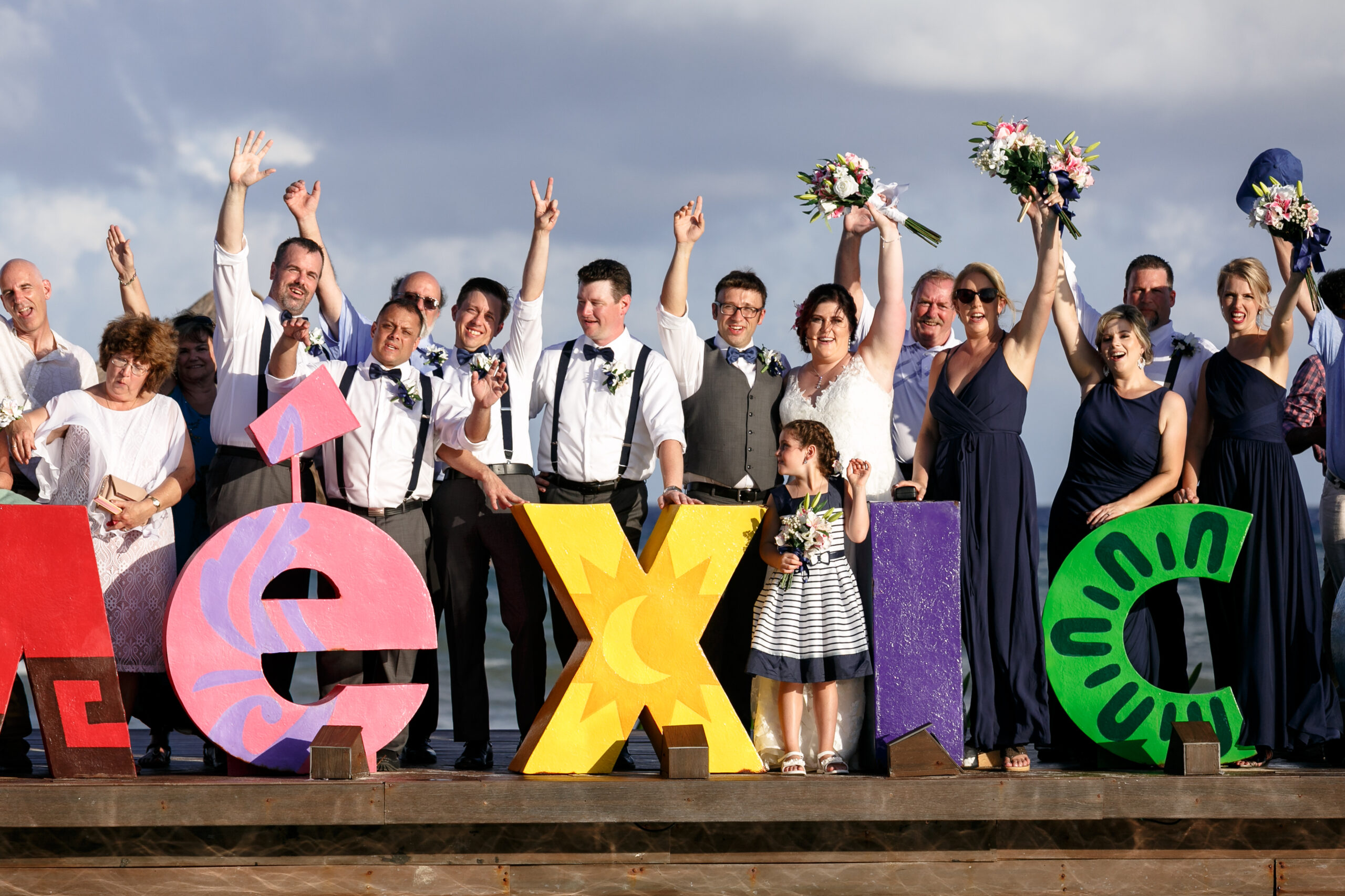 Happy newlyweds and guests cheer behind MEXICO sign