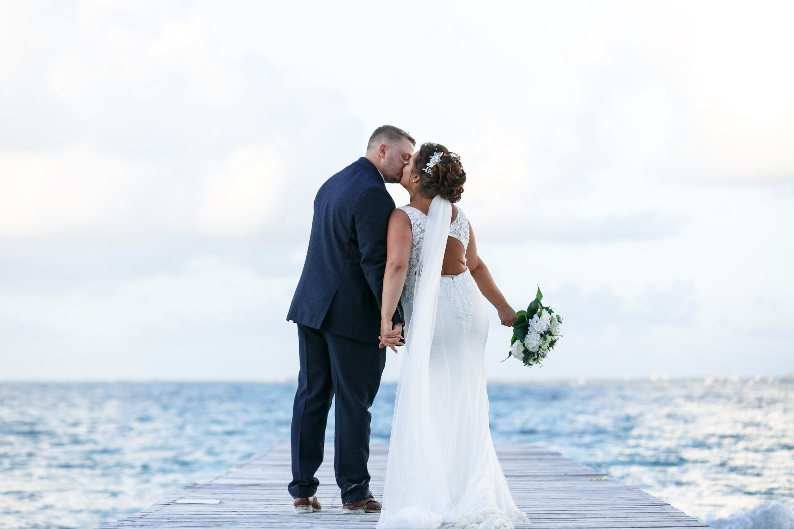 Newlyweds kiss on pier overlooking beautiful ocean