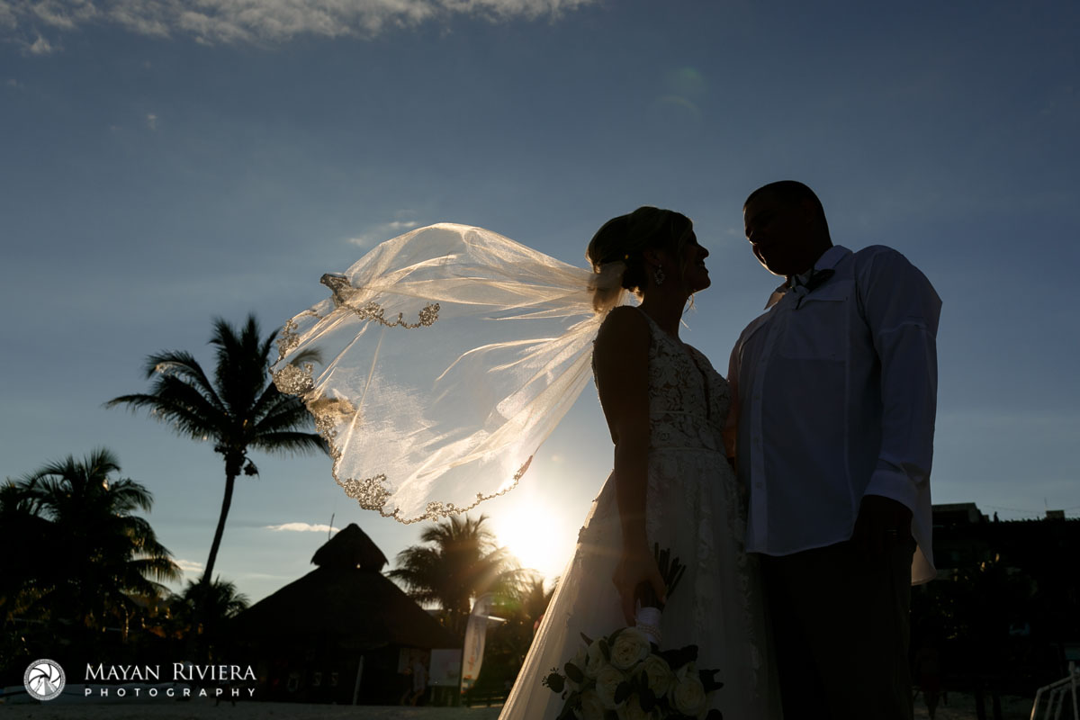 Bride + Groom stand together, their silhouette showing her veil lit by the setting sun