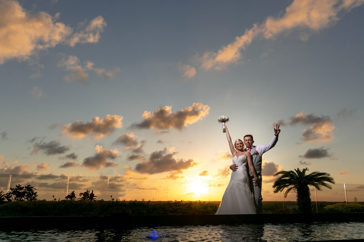 Newlyweds cheer silhouetted with the sunset