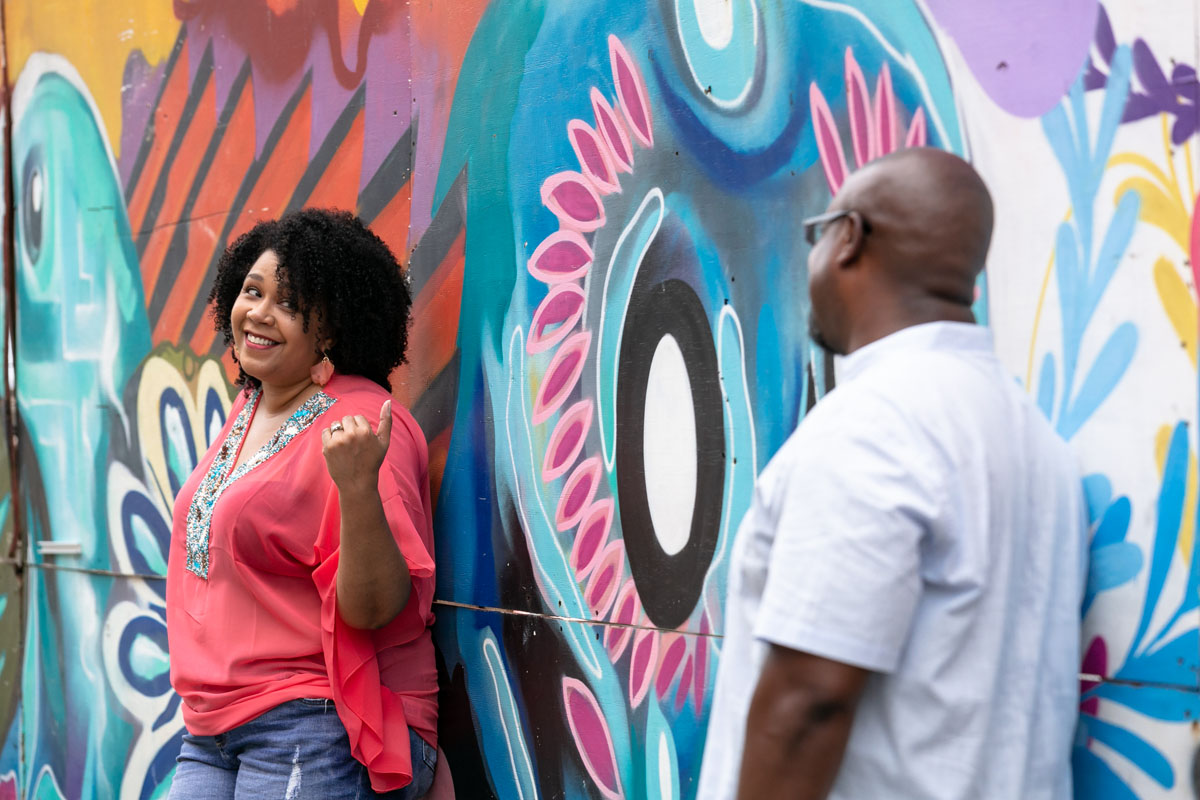 Wife playfully beckons husband in front of graffiti wall