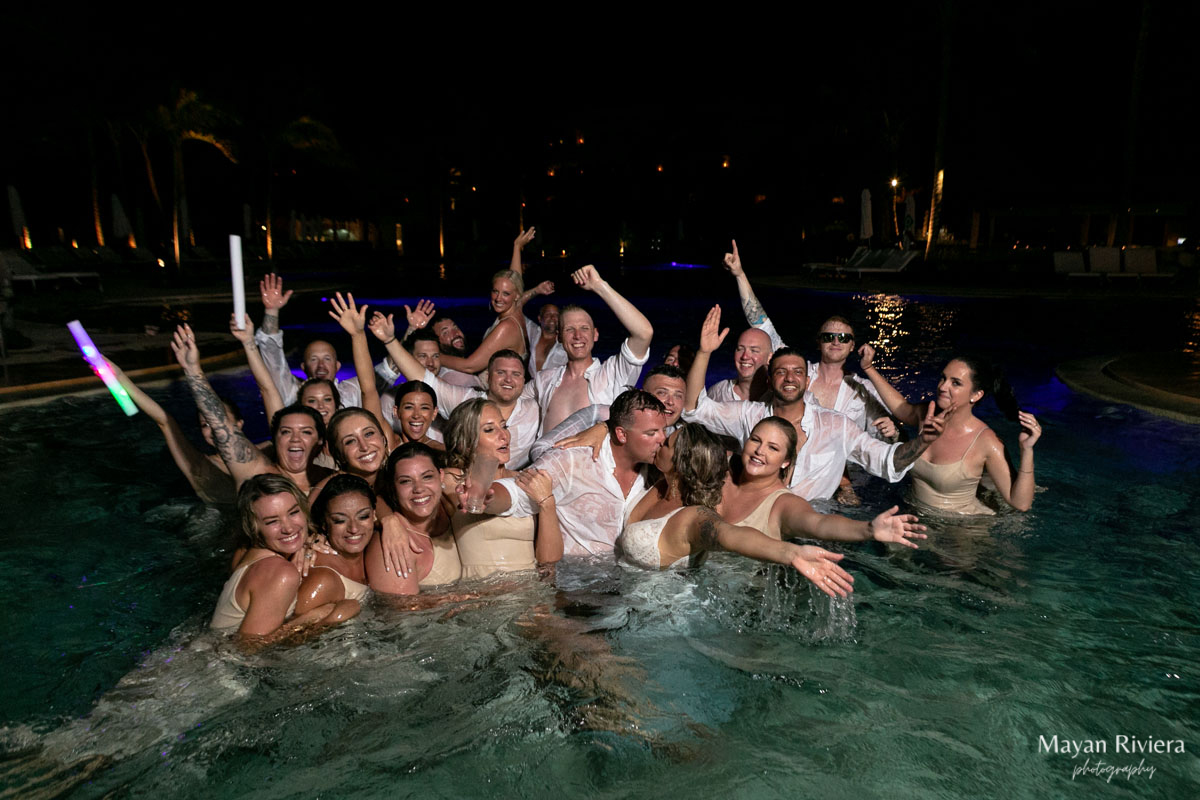 Newlyweds kiss surrounded by cheering wedding party splashing in cenote