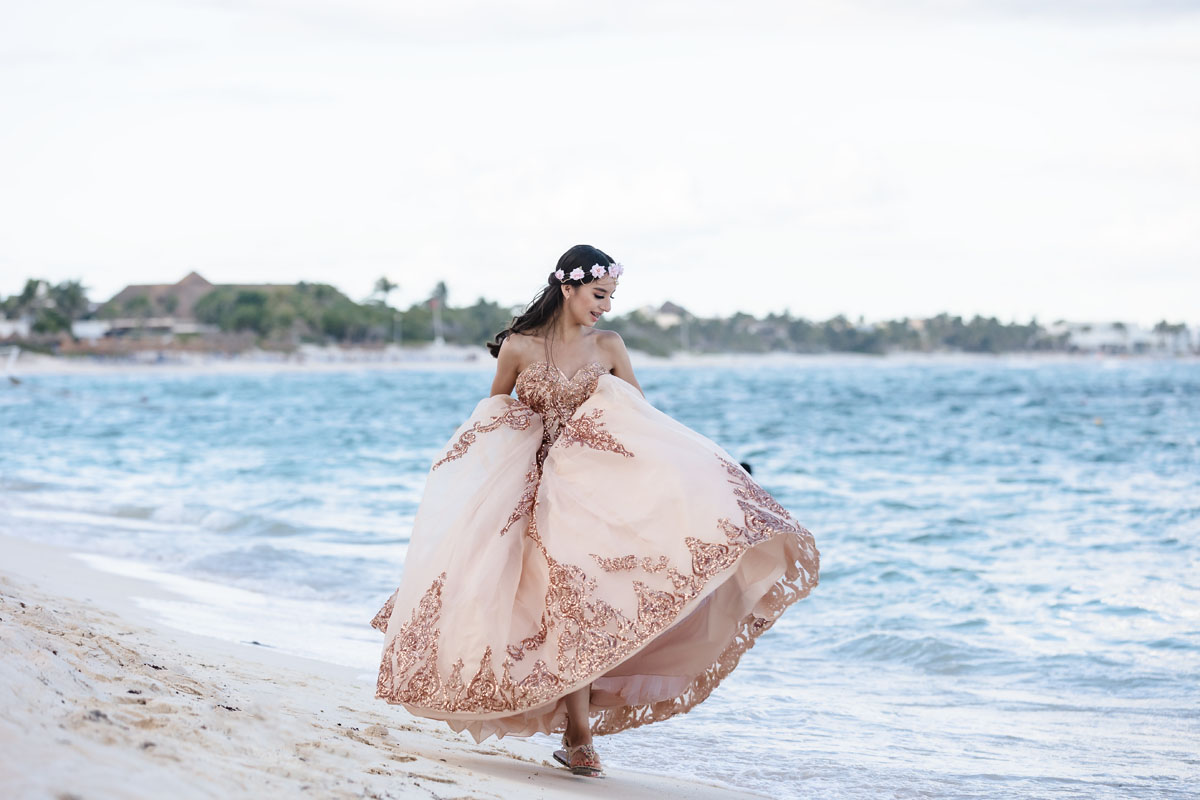 Happy Quinceanera girl twirls her gown, dancing on the beach