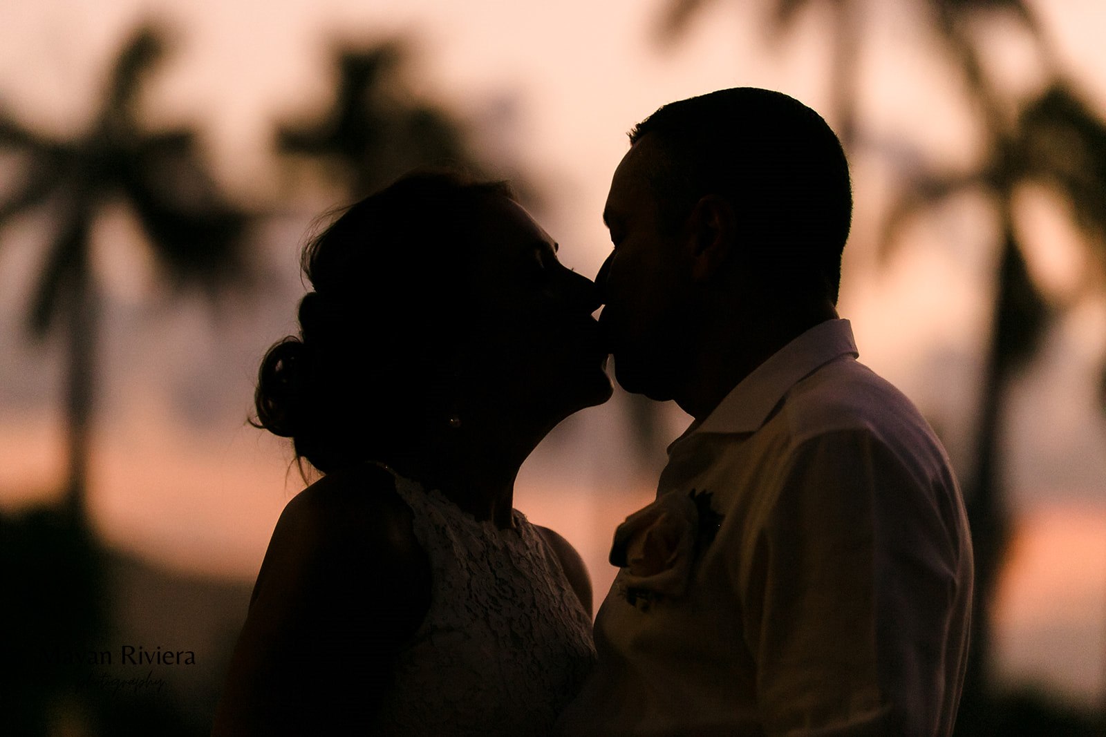 Newlyweds kiss, silhouetted against a stunning sunset