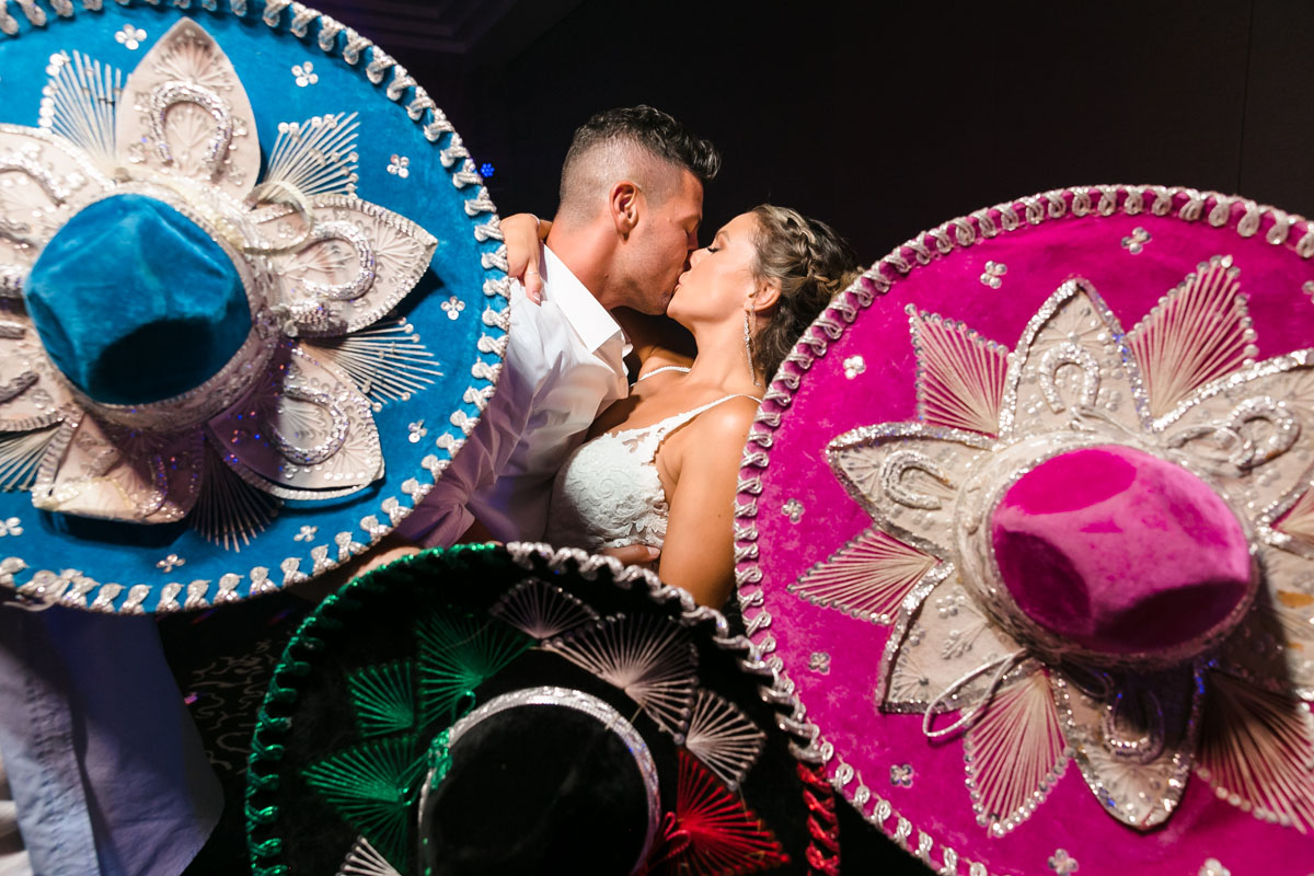 Newlyweds kiss behind screen of Mexican sombreros