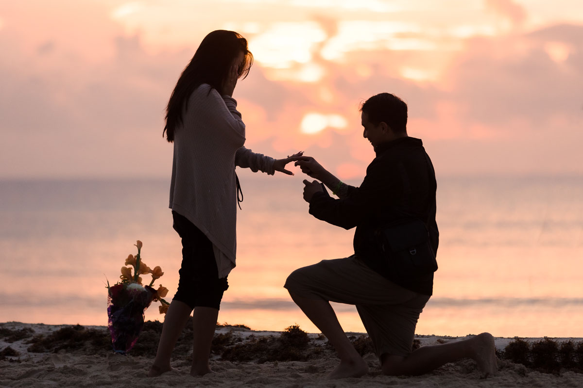 Boyfriend down on one knee to surprise his girlfriend at sunrise on the beach