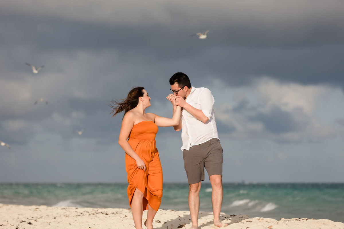 Husband kisses his happy wife's hand under a dramatic sky