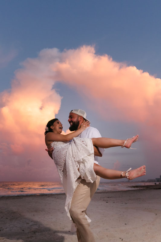 Newlywed husband twirls bride on the beach at sunset