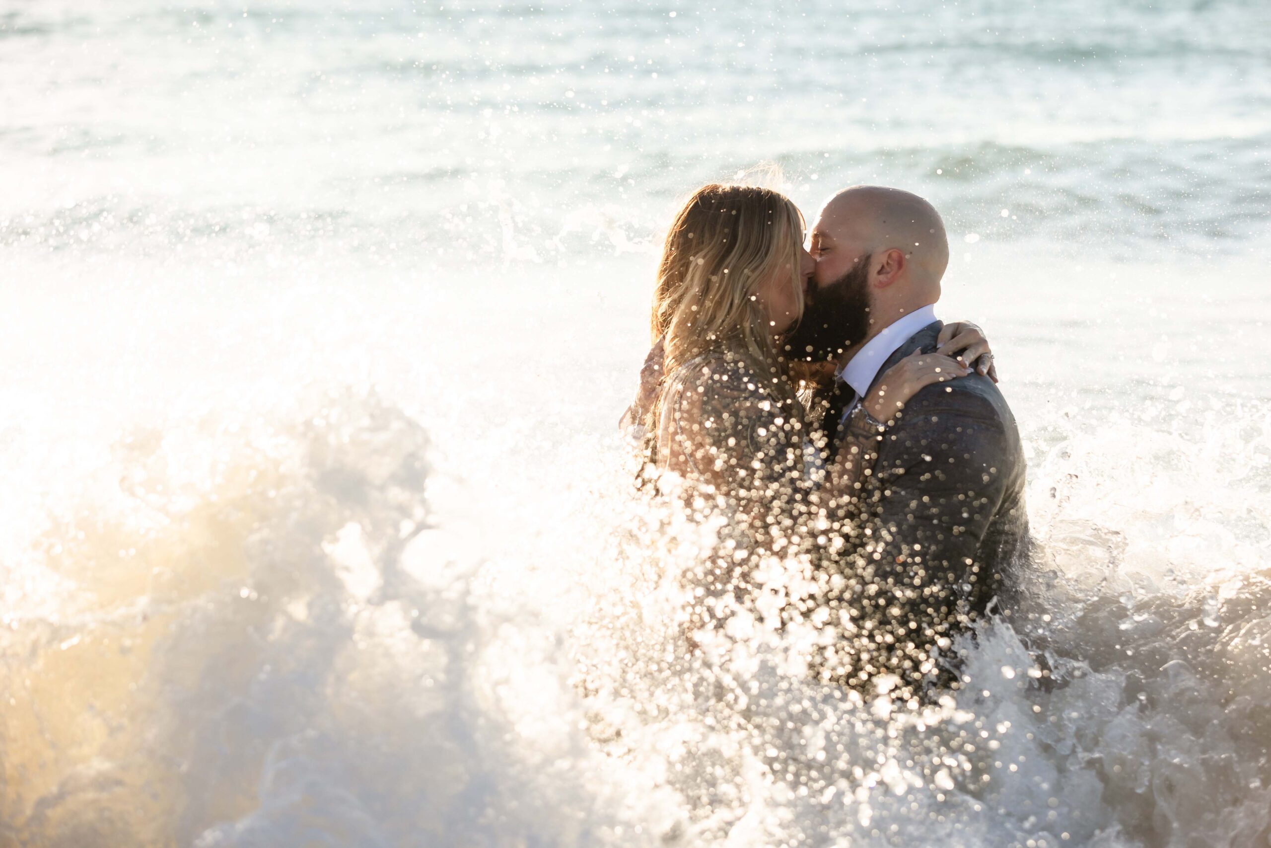 Newlyweds kiss, sprayed by a wave