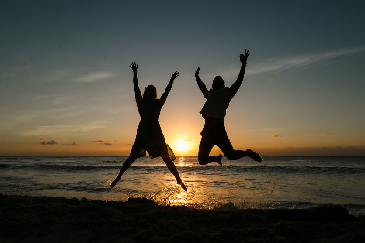 Newly engaged couple jump for joy on beach at sunrise