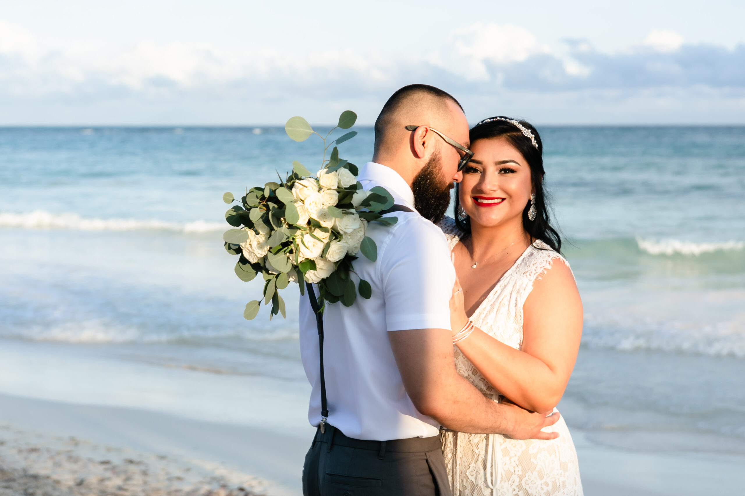 Newlywed bride beams in the arms of her groom on the beach