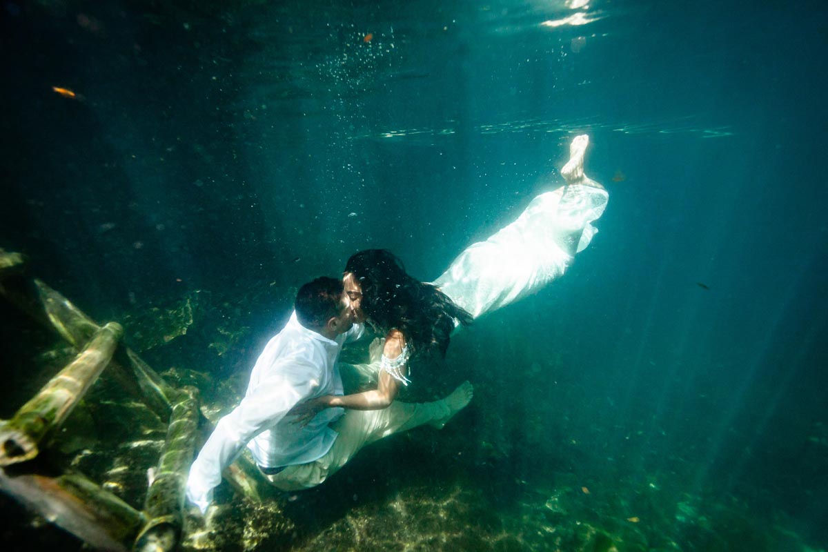 Newlyweds kiss immersed in the crystal clear water of a cenote
