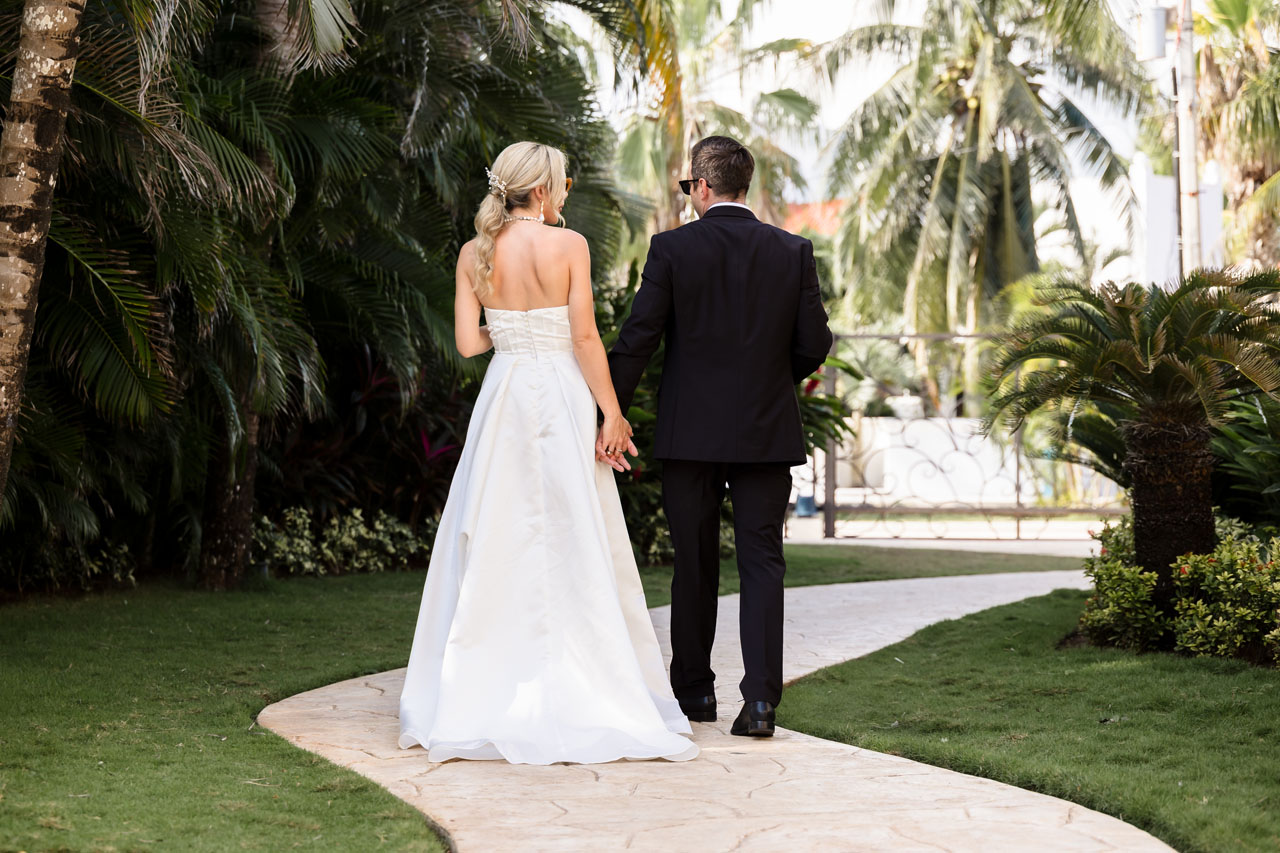 Wedding couple strolls on jungle garden path holding hands