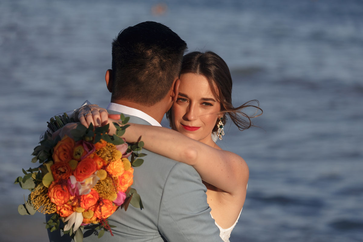 BrideSmilesOverHusbandsShoulderLitBySunset