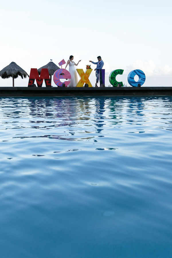 NewlywedsPointToEachOtherByMexicoSign