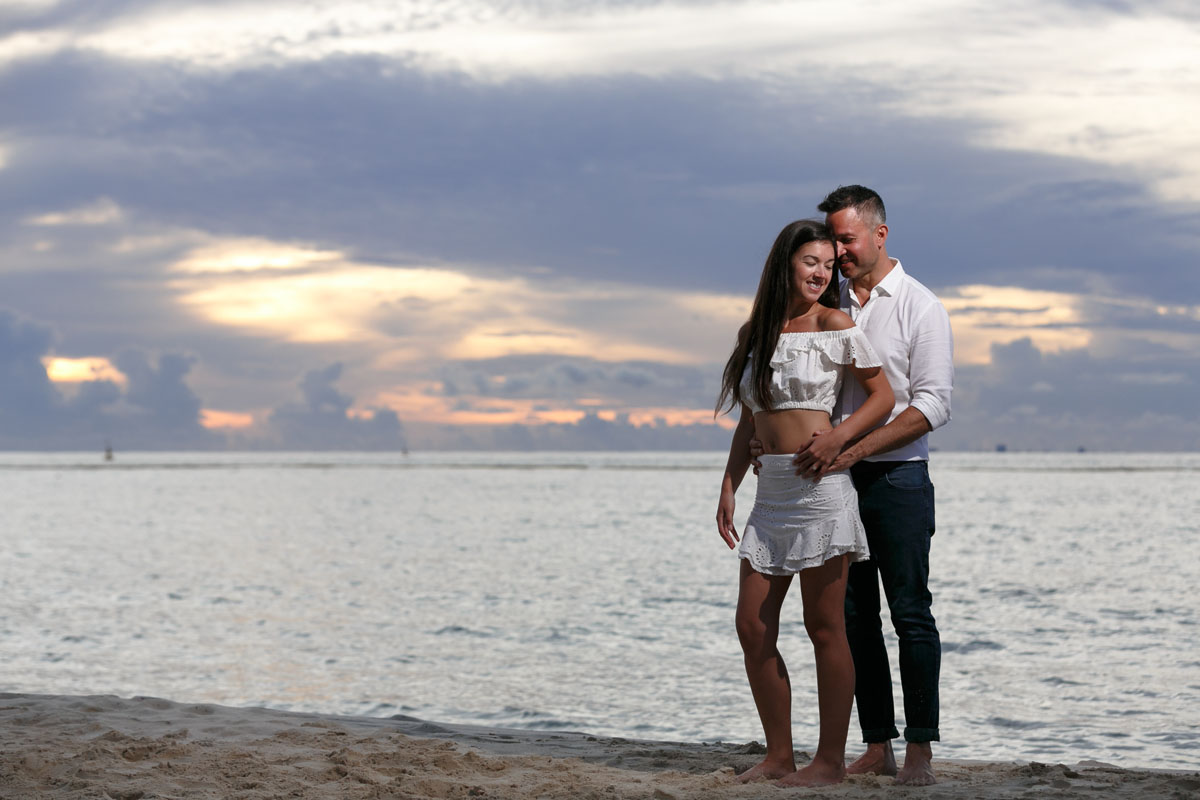 NewlyEngagedCouplePoseOnPdCBeachAtSunrise
