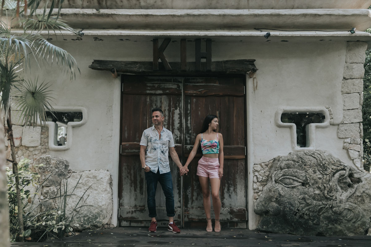 NewlyEngagedCoupleHoldHandsByWoodenDoor
