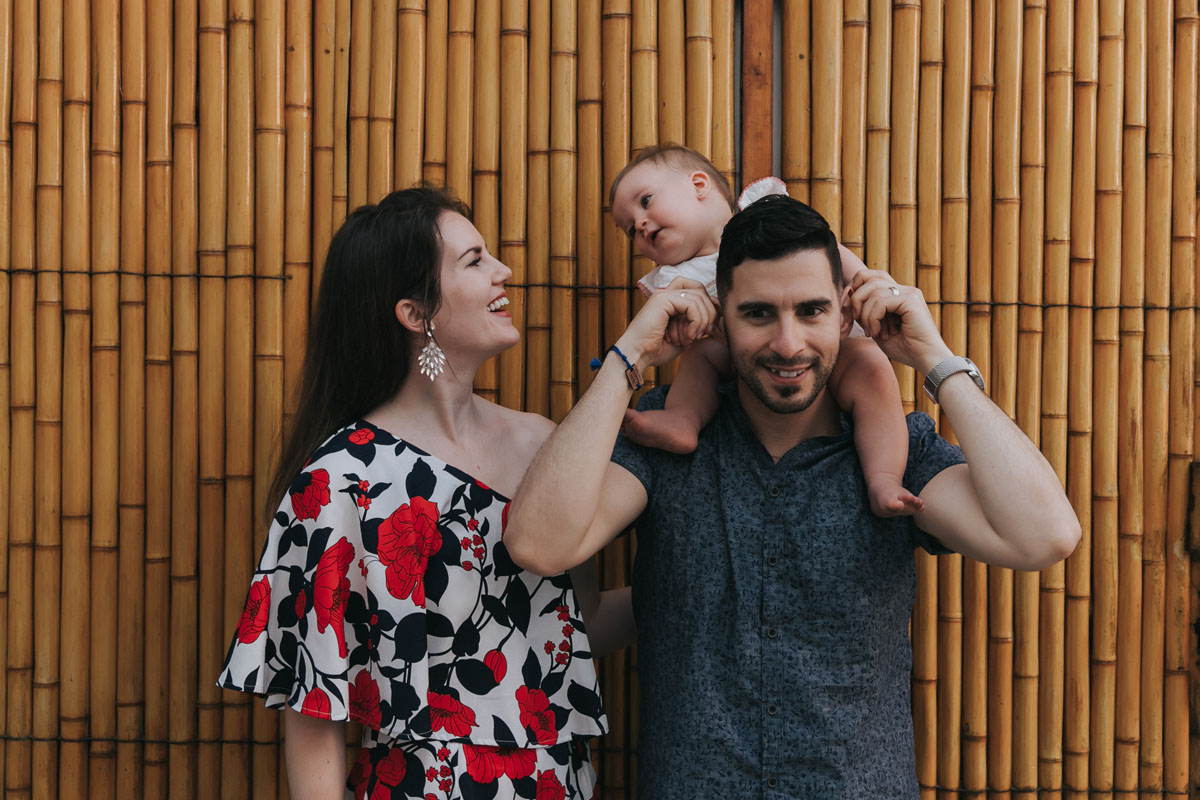 SmilingParentsPoseWithBabyByBambooWall
