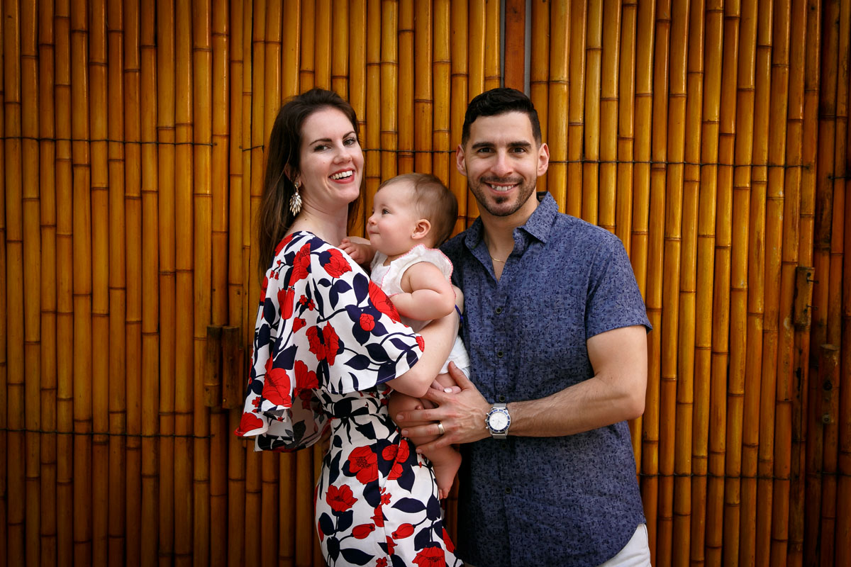 SmilingParentsPoseWithBabyByBambooWall