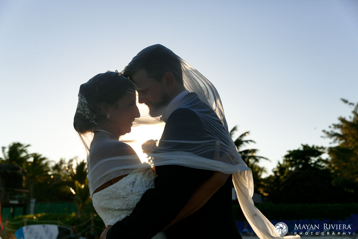NewlywedsNuzzleOnBeachUnderVeil