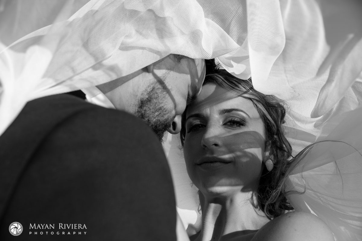 NewlywedsNuzzleOnBeachUnderVeil