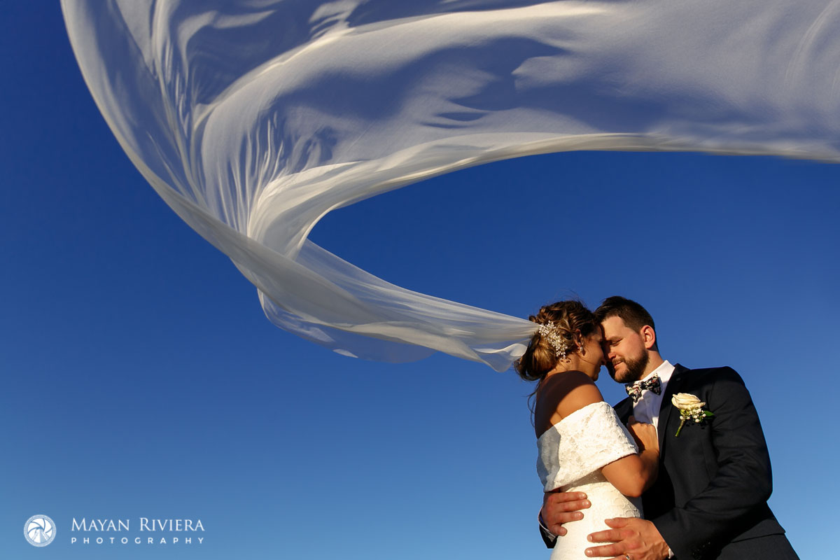 NewlywedsNuzzleOnBeachUnderVeil