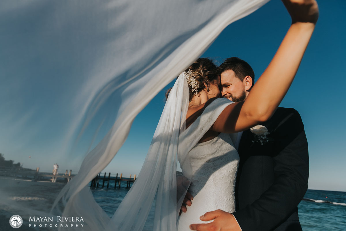 NewlywedsNuzzleOnBeachUnderVeil