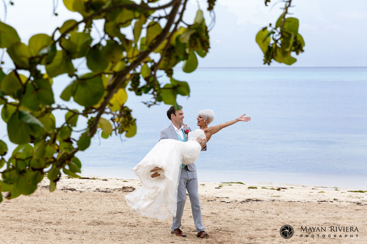 Groom carries his cheering bride in his arms on the beach