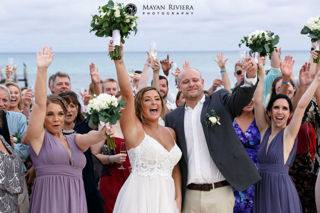 CheeringWeddingGuestsWithNewlywedsInBeachDroneShot