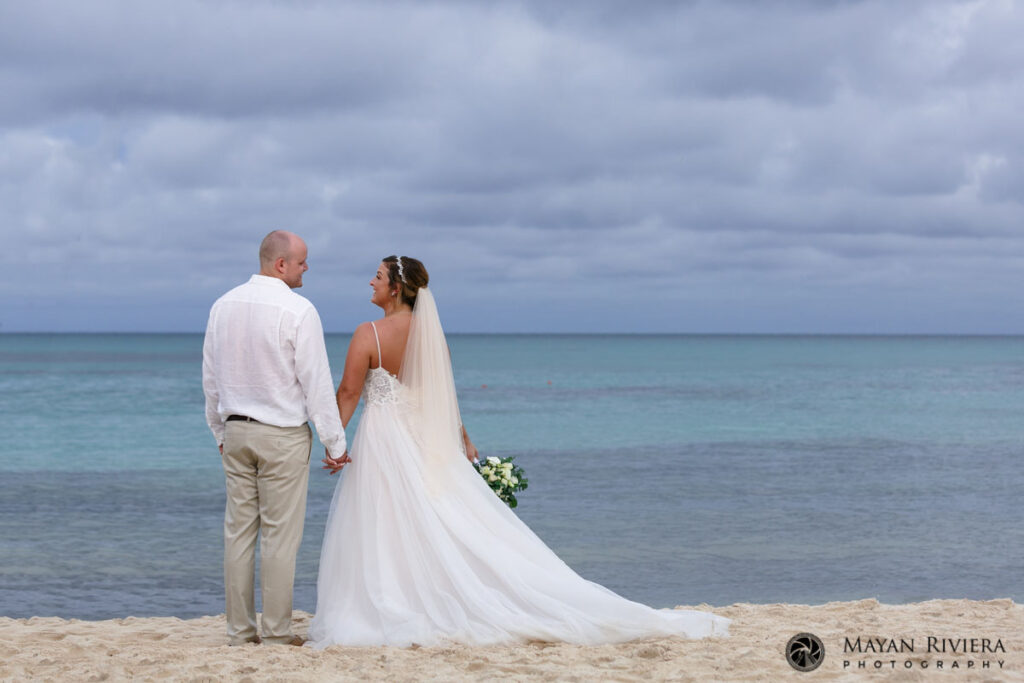 NewlywedsStandHandInHandOnBeach