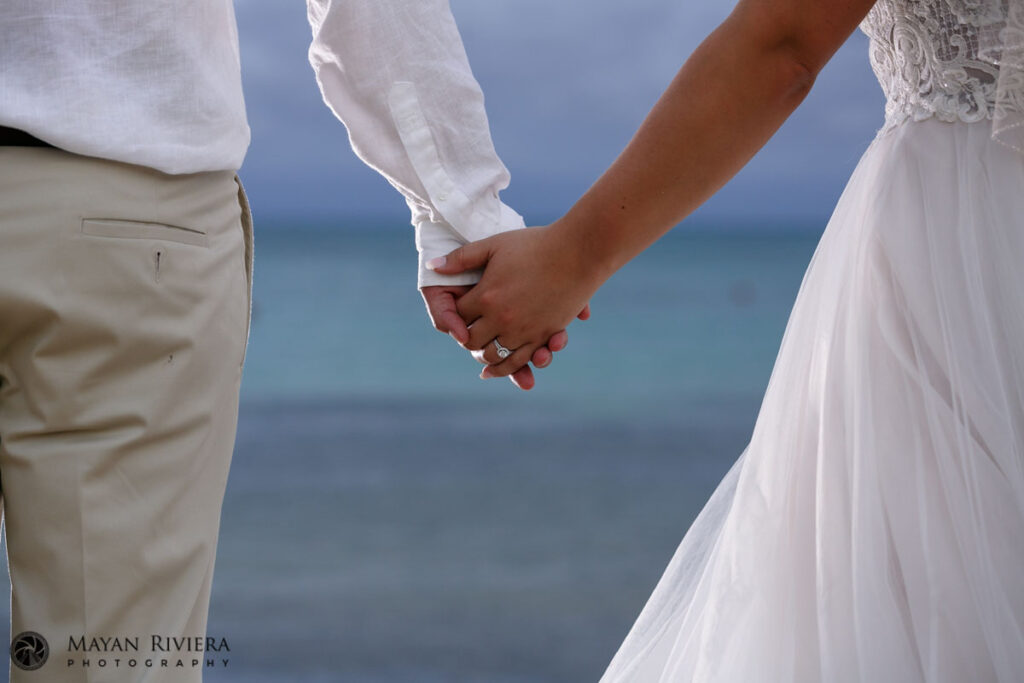 NewlywedsStandHandInHandOnBeach