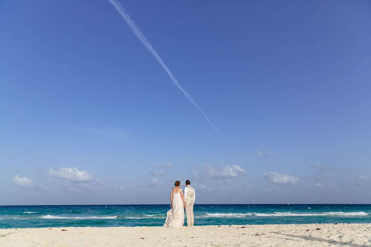 NewlywedsStandOnBeachLookingOutToSea