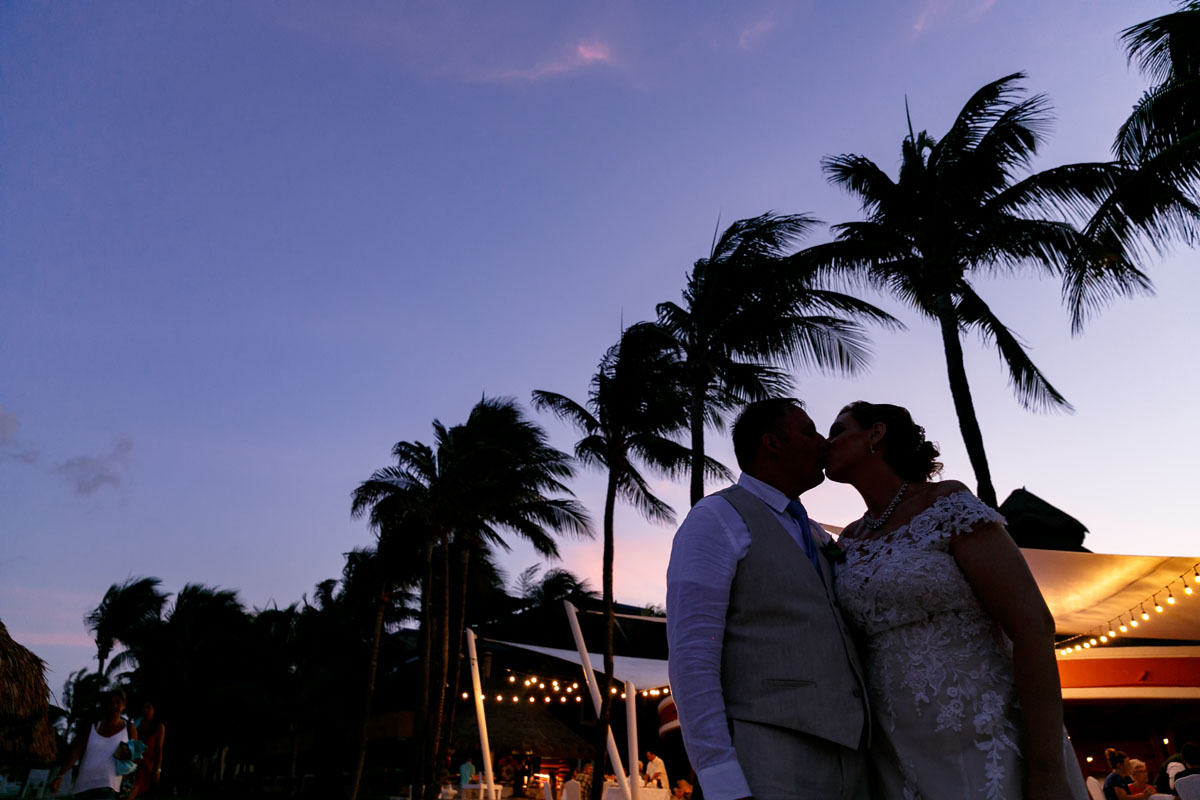 Newlyweds kiss shilouetted by a pastel sky
